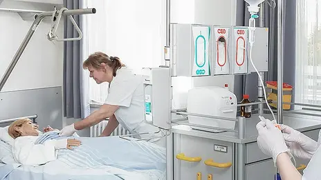 Eine Mitarbeiterin der Dermatologie kümmert sich um eine Patientin im Bett.