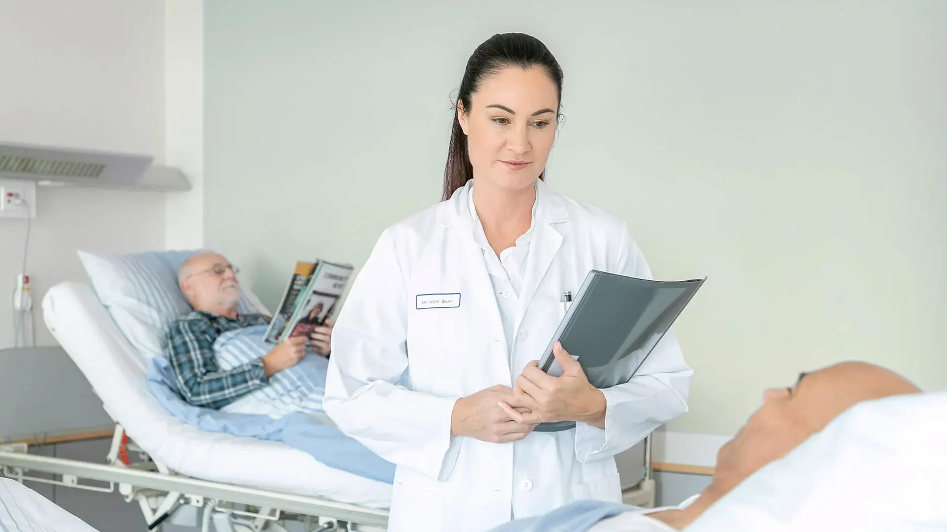 Eine Ärztin steht neben einem Patientenbett und unterhält sich mit einem Patienten. 