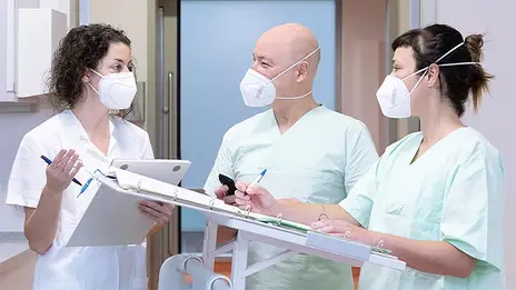 Drei Mitarbeitende stehen neben einem Patientenbett und besprechen sich. 