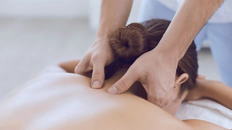 Ein Mitarbeiter massierte eine Patientin am Nacken. Sie liegt auf einer Massageliege. 