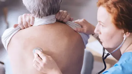 Eine Ärztin horcht mit dem Stethoskop den Rücken eines Patienten ab.