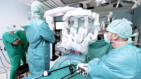 Der Operations-Roboter besteht aus einer Steuerkonsole, an der ein Chirurg sitzt, und einer patientenseitigen Robotikeinheit mit vier Armen und einem Videoturm für die Steuerung der Kamera. 