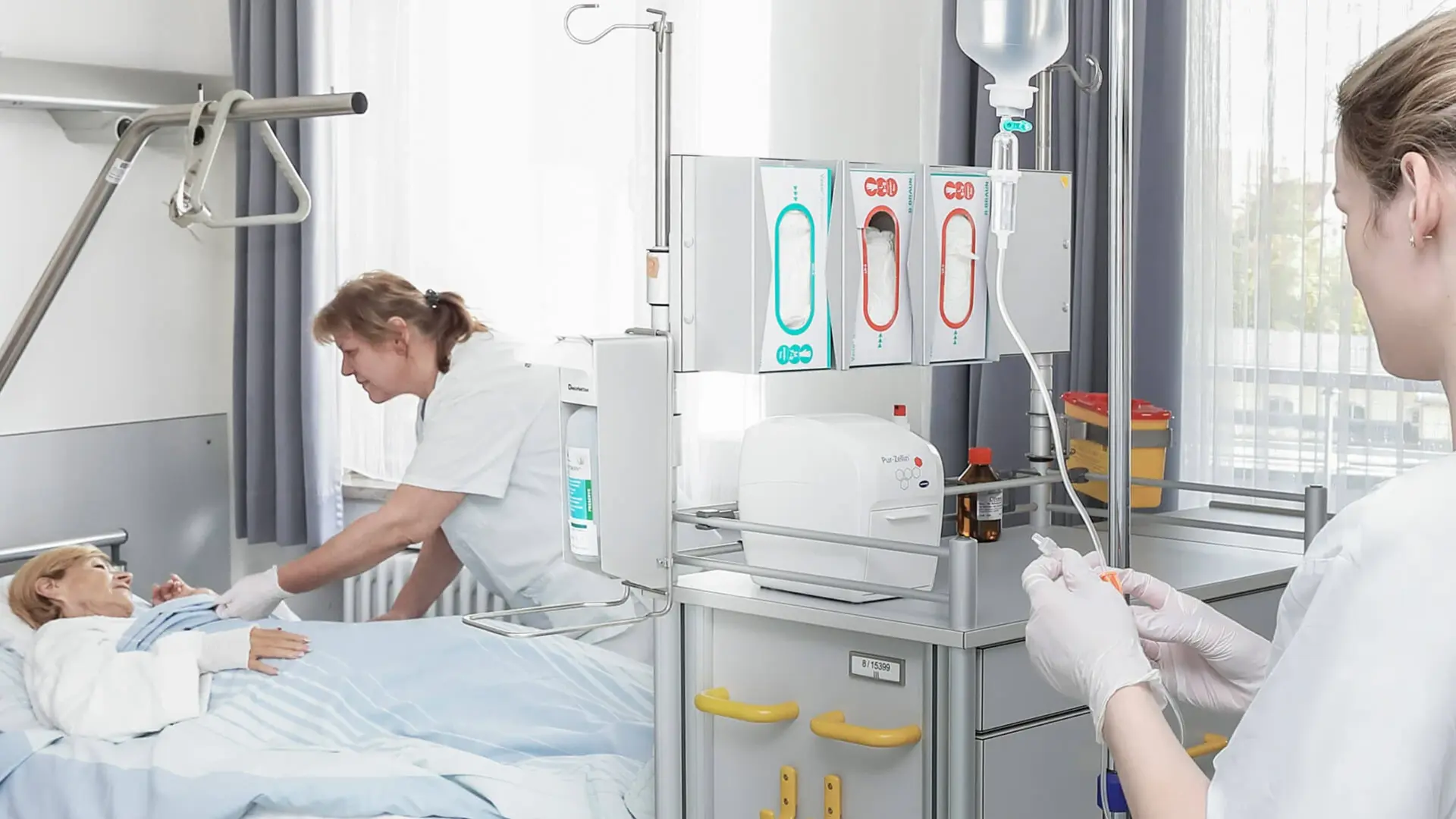 Patientin liegt im Bett und wird von zwei Pflegekräften versorgt.