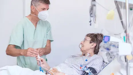 Oberarzt, Dr. Dirk Risack spricht mit einer Patientin im Bett.  