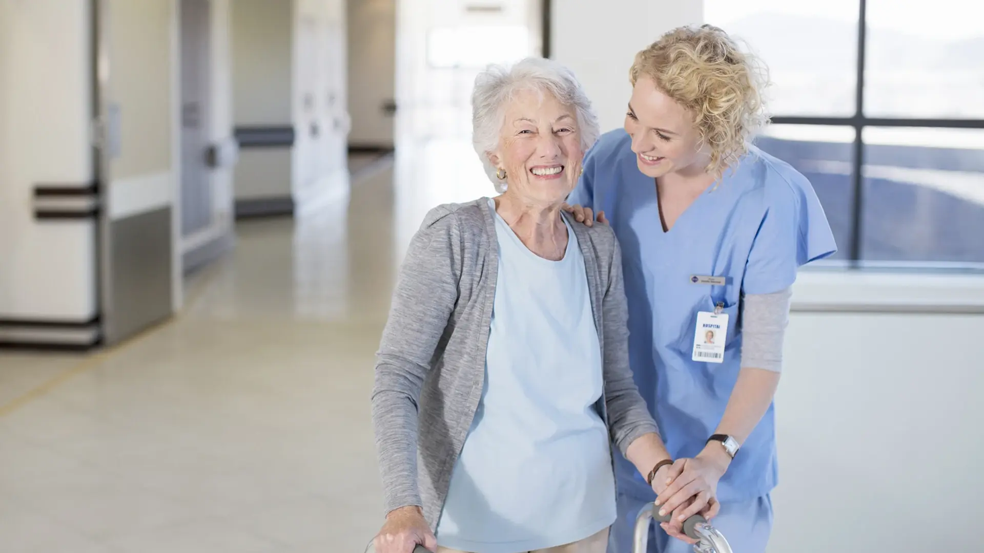 Eine Mitarbeitende begleitet eine ältere Patienten durch den Flur.