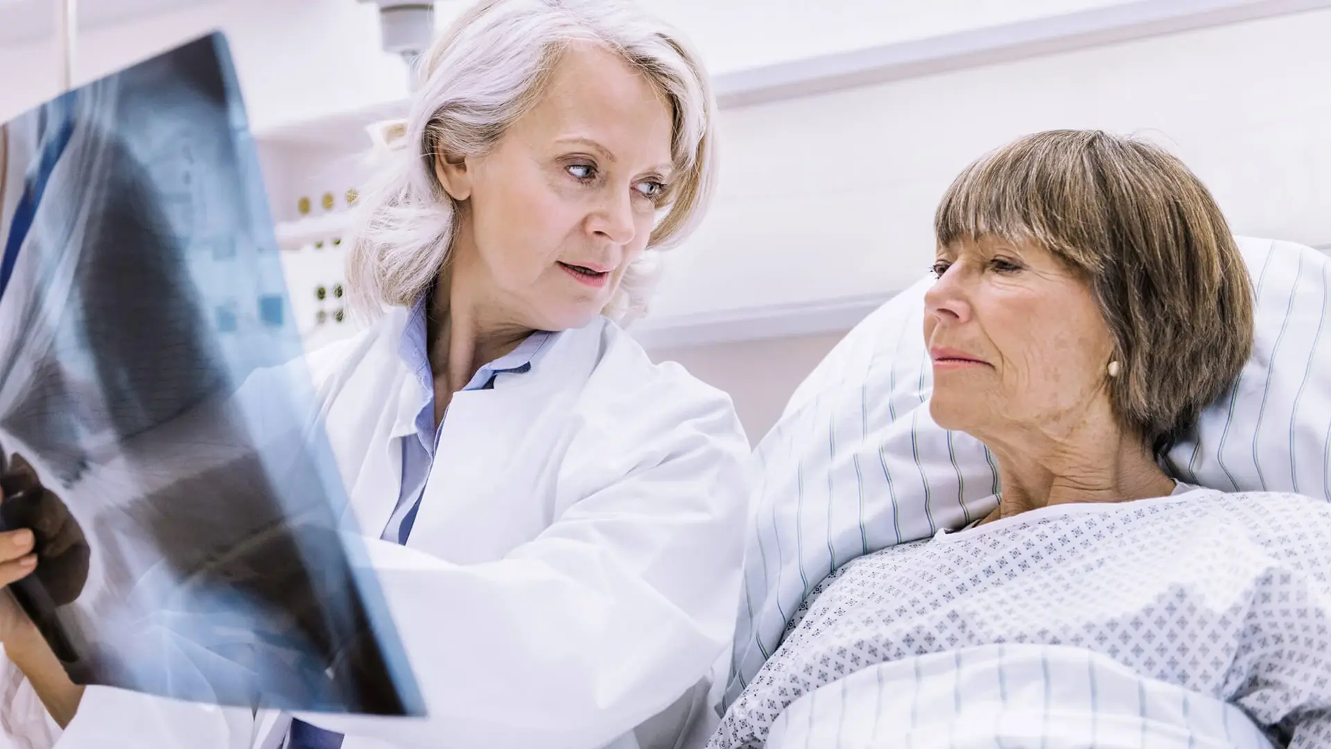 Eine Ärztin bespricht Lungenröntgenaufnahmen mit ihrer im Bett liegenden Patientin.
