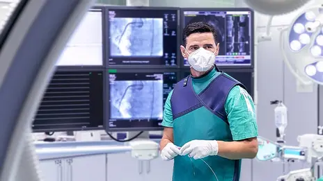 Fadil Ademaj, Oberarzt, steht während eines Eingriffs vor mehreren Monitoren. 
