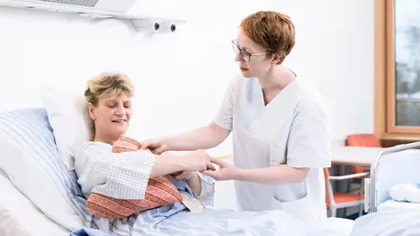  Eine Mitarbeiterin legt einer Brustkrebspatientin ein Herzkissen unter den Arm 