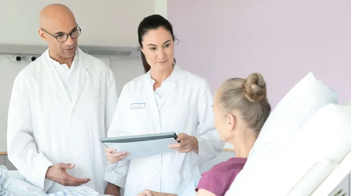 Zwei Ärzte sprechen mit einer Patientin im Bett