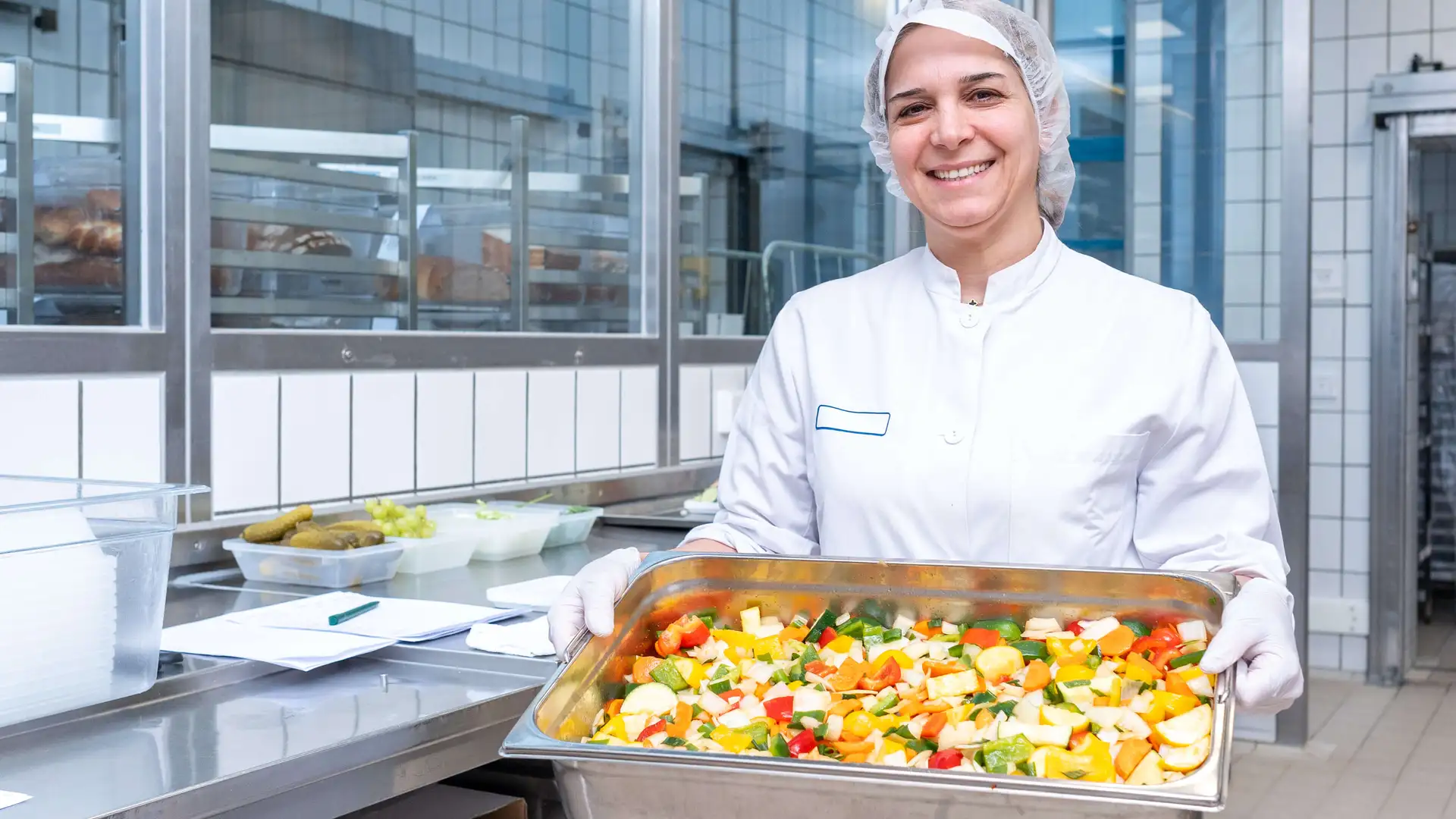 Eine Mitarbeitende der Küche zeigt ein Gemüsegericht. 