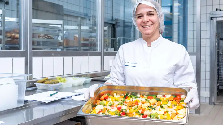 Eine Mitarbeitende der Küche zeigt ein Gemüsegericht. 