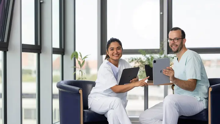 Das Symbolbild zeigt eine Kollegin und einen Kollegen. Beide haben ein iPad in der Hand. 
