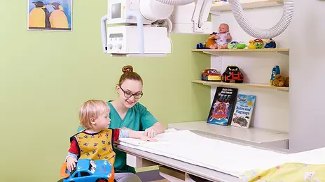 Eine Mitarbeiterin der Kinder-Radiologie bereitet einen kleinen Jungen auf die Röntgenaufnahme vor. 