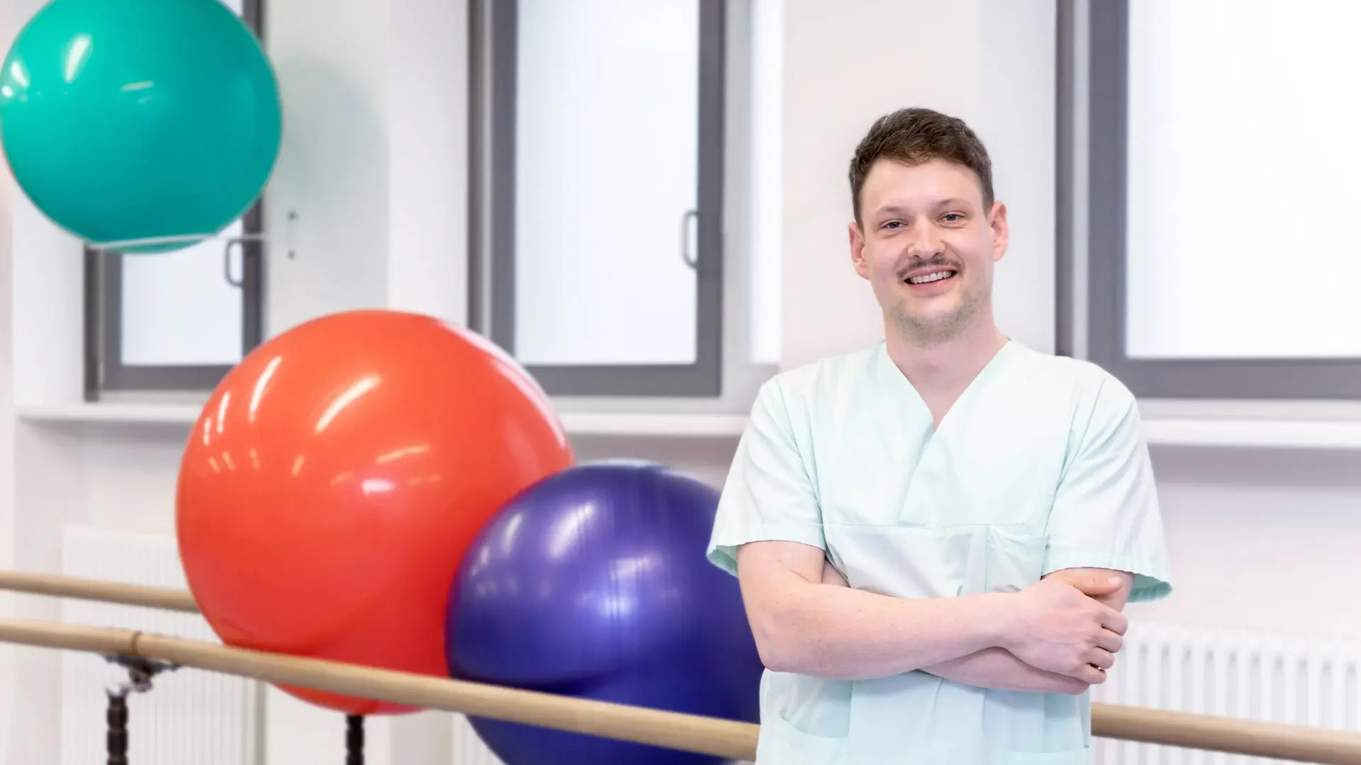 Moritz Rößner, Physiotherapeut, steht vor mehreren Gymnastikbällen. 