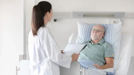 Eine Ärztin unterhält sich mit einem Patienten im Bett.