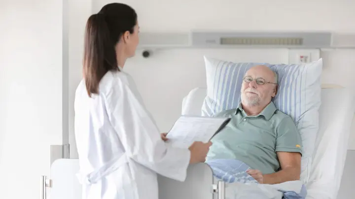 Eine Ärztin unterhält sich mit einem Patienten im Bett.