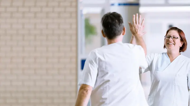 Zwei Mitarbeitende klatschen sich am Flur in die Hände