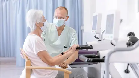 Ein Mitarbeiter der Tagesklinik erklärt einer älteren Patientin ein Trainingsgerät. 