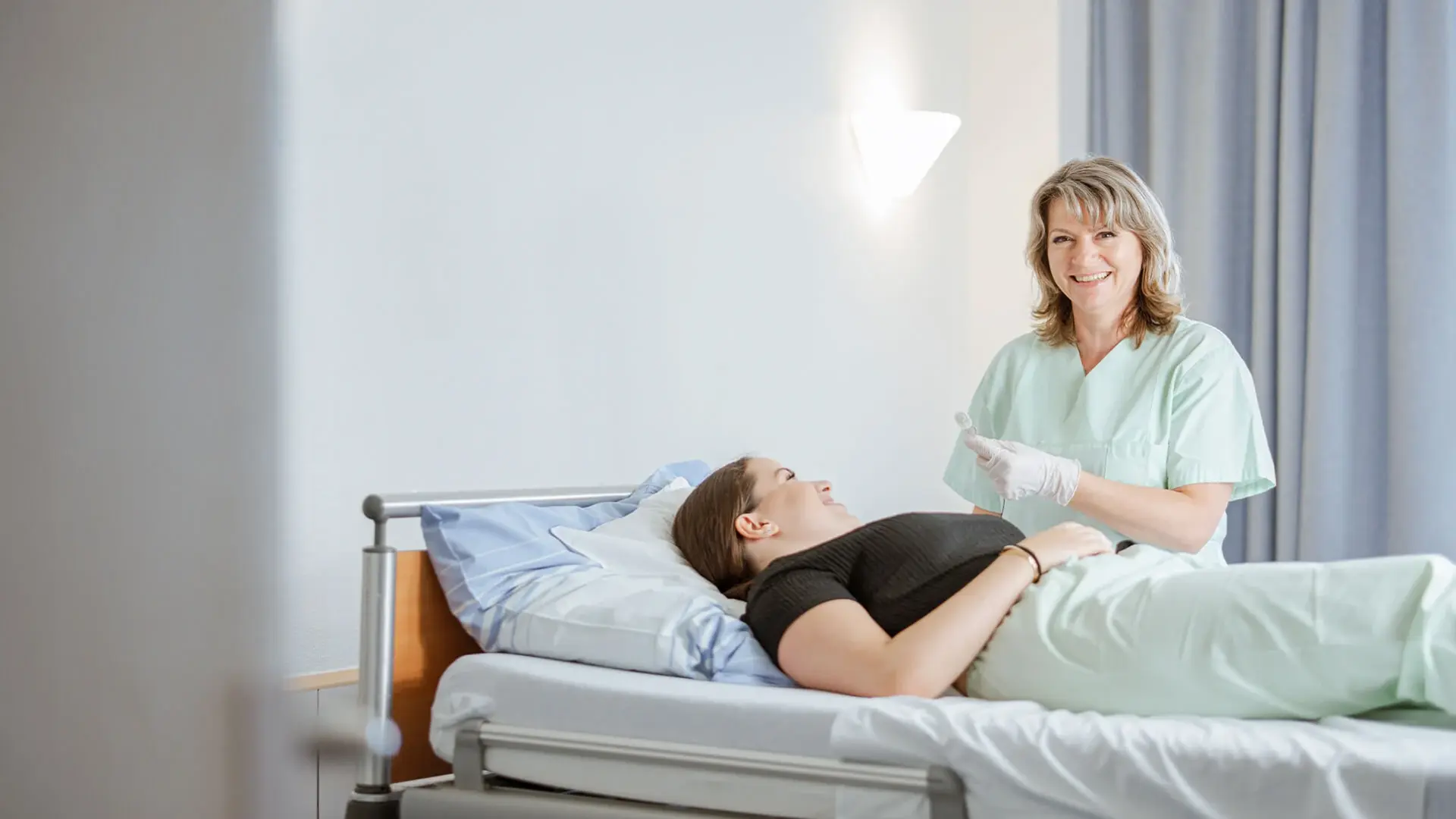 Eine Pflegekraft versorgt die Patientin im Bett.