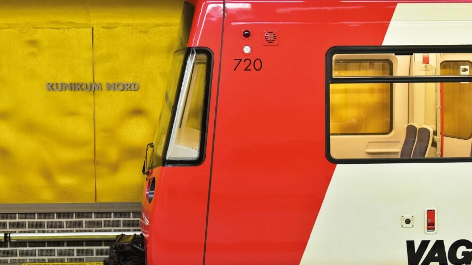 Eine goldene U-Bahn-Station mit der Aufschrift „Klinikum Nord“ an der Wand. Im Vordergrund steht ein rot-weißer Zug der VAG Nürnberg, dessen Fenster und Sitzplätze sichtbar sind