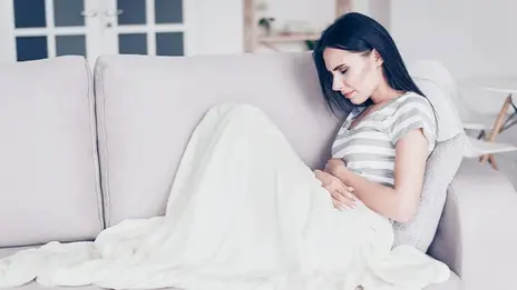 Auf dem Sofa liegende Frau mit Schmerzen im Bauchbereich