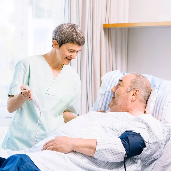 Eine Mitarbeitende erklärt dem Patienten die Fernbedienung des Krankenbetts.
