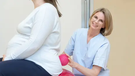Eine Hebamme stützt eine schwangere Frau auf dem Gymnastikball.