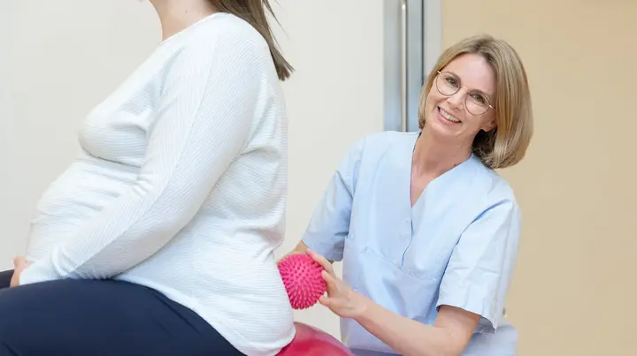 Eine Hebamme stützt eine schwangere Frau auf dem Gymnastikball.