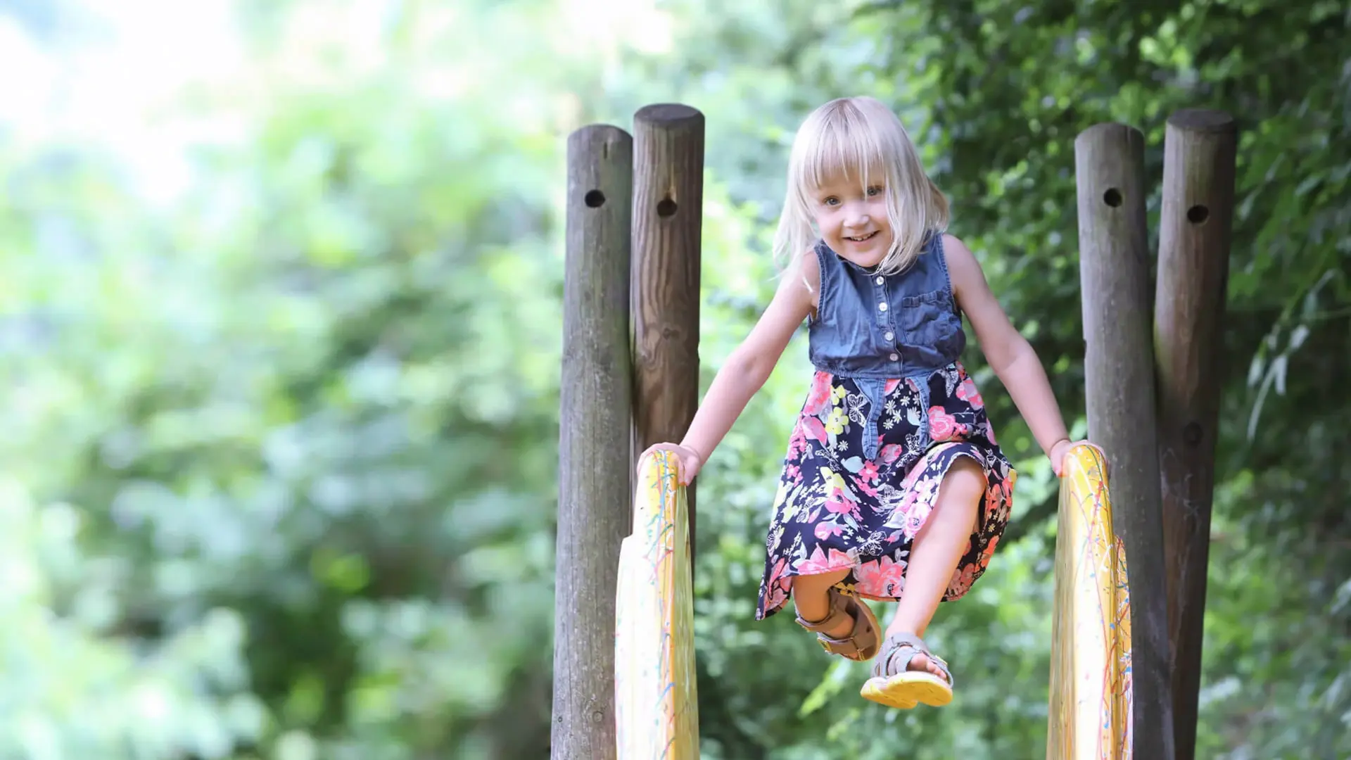 Die 3-jährige Merle stützt sich mit den Händen auf einer Rutsche ab. Sie lacht dabei in die Kamera.
