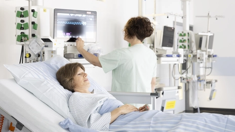 Eine Patientin liegt im Aufwachraum der Gastroenterologie, wo sie durch eine Mitarbeiterin betreut wird.