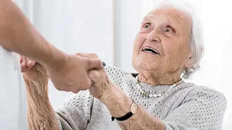 Das Symbolbild zeigt eine ältere Dame, die einen Mitarbeitenden anlacht. Sie halten Händchen. 