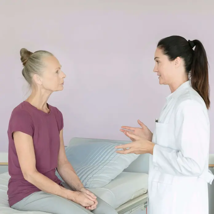 Eine Ärztin unterhält sich mit einer Patientin. Sie sitzt an der Bettkante.