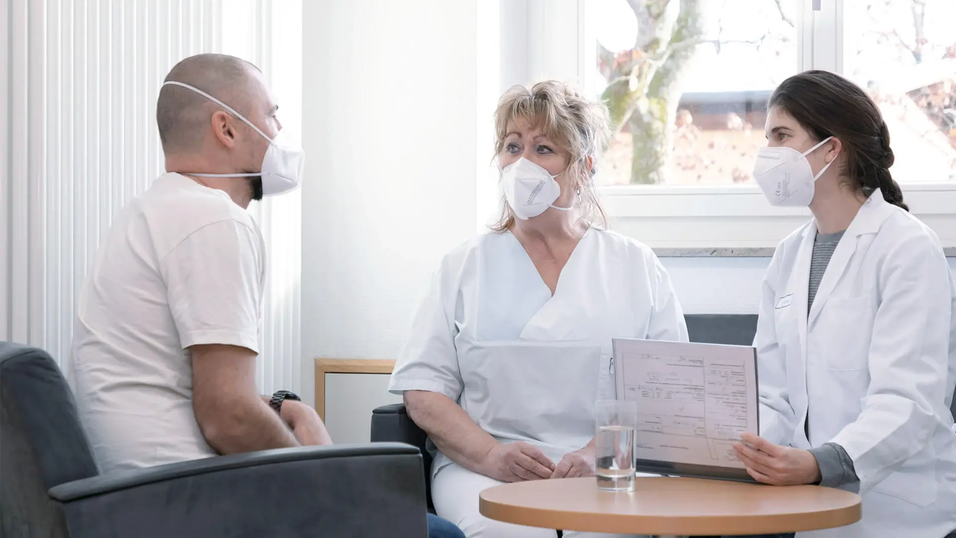 Zwei Mitarbeiterinnen der Psychiatrie unterhalten sich mit einem Patienten. 