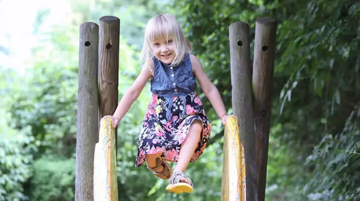 Die damals 3-jährige Merle stützt sich mit den Händen auf einer Rutsche ab. Sie lacht dabei in die Kamera. 