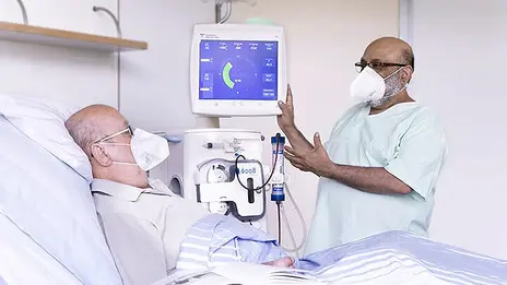 Ein Mitarbeiter der Nephrologie spricht mit einem Patienten im Bett. 