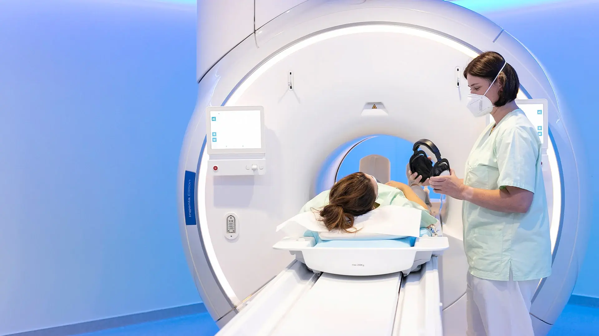 Eine Mitarbeiterin der Radiologie setzt einer Patientin kurz vor der Untersuchung mittels Computertomographie die Kopfhörer auf. 