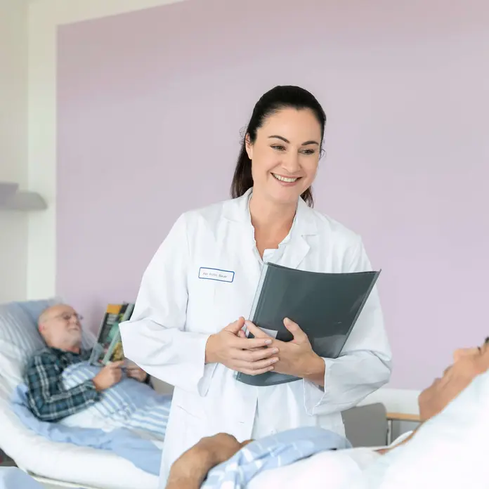 Eine weibliche Ärztin spricht mit einem Patienten im Bett.