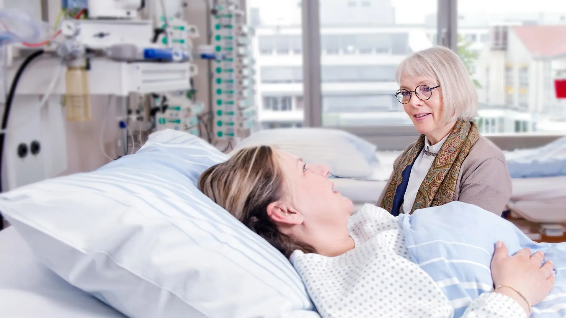 Eine Mitarbeitende der Seelsorge spricht mit einer Patientin im Bett. 