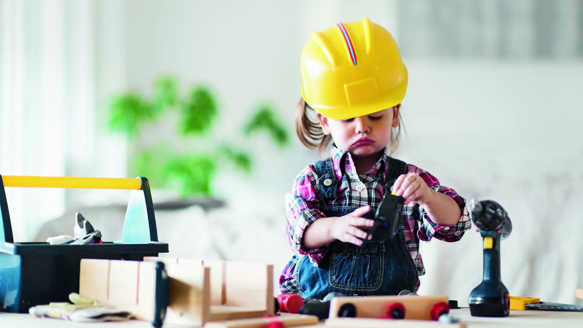 Ein kleines Mädchen baut mit Bauklötzen. Sie hat einen gelben Baustellenhelm an. 