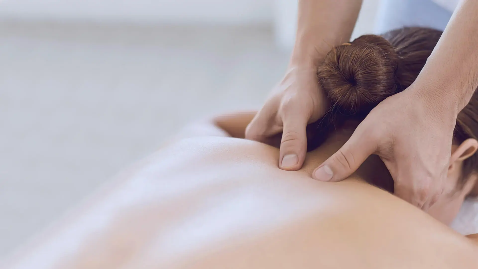 Ein Mitarbeiter massierte eine Patientin am Nacken. Sie liegt auf einer Massageliege. 