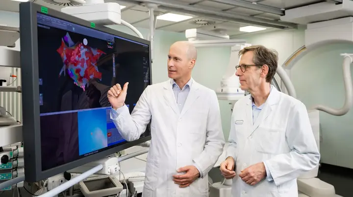 Zwei Ärzte stehen vor einem großen Monitor und besprechen sich