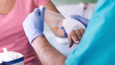 Ein Mitarbeiter der Geriatrie verbindet die Hand einer Patientin. 