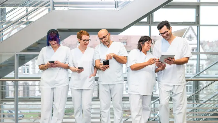 Auf dem Bild sind fünf Mitarbeitende des Klinikums. Sie lesen die neusten Infos auf den Smartphones.