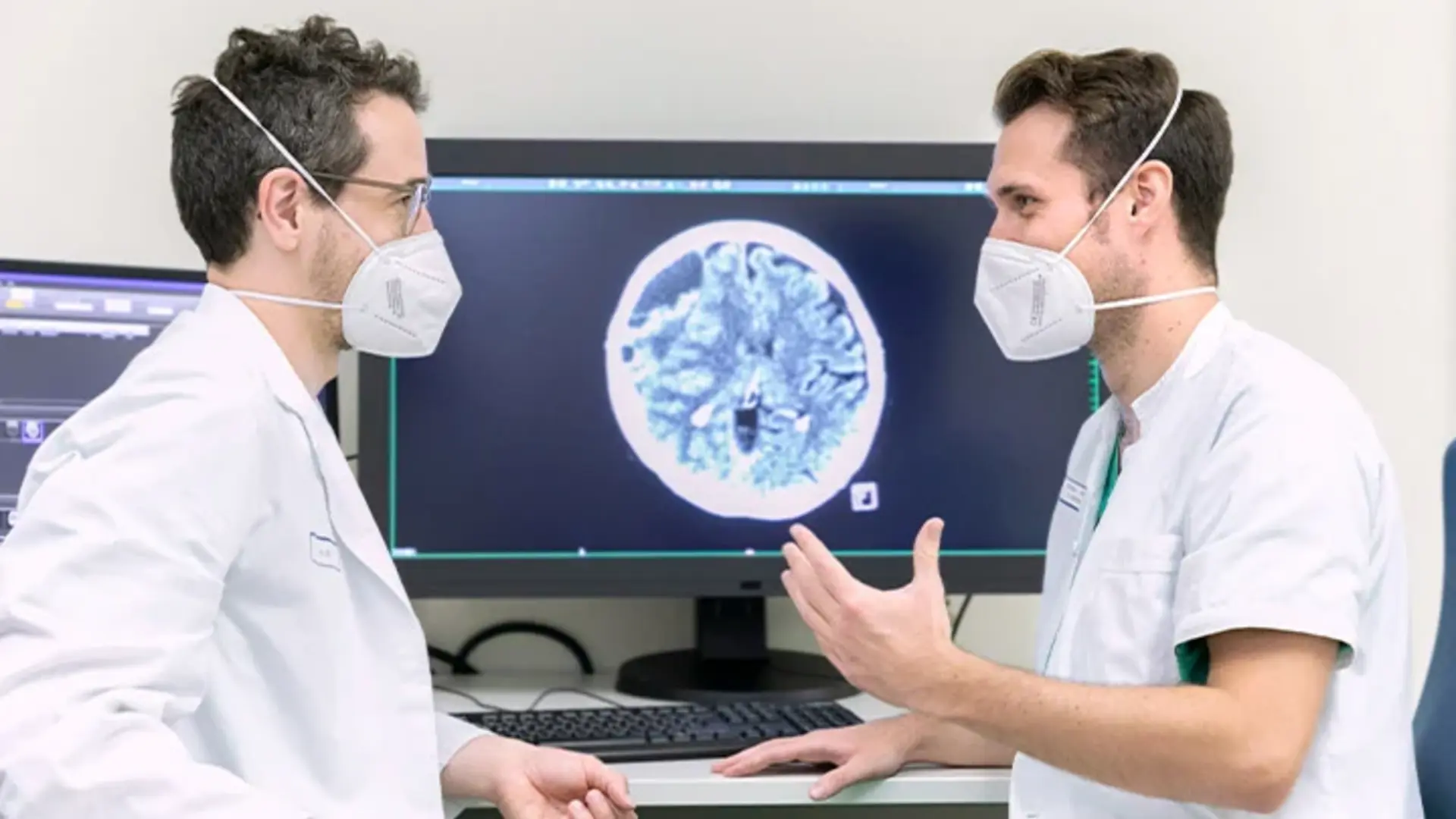 Zwei Mitarbeitende der Neuroradiologie besprechen Untersuchungsergebnisse. Sie sitzen vor mehreren Bildschirmen. 