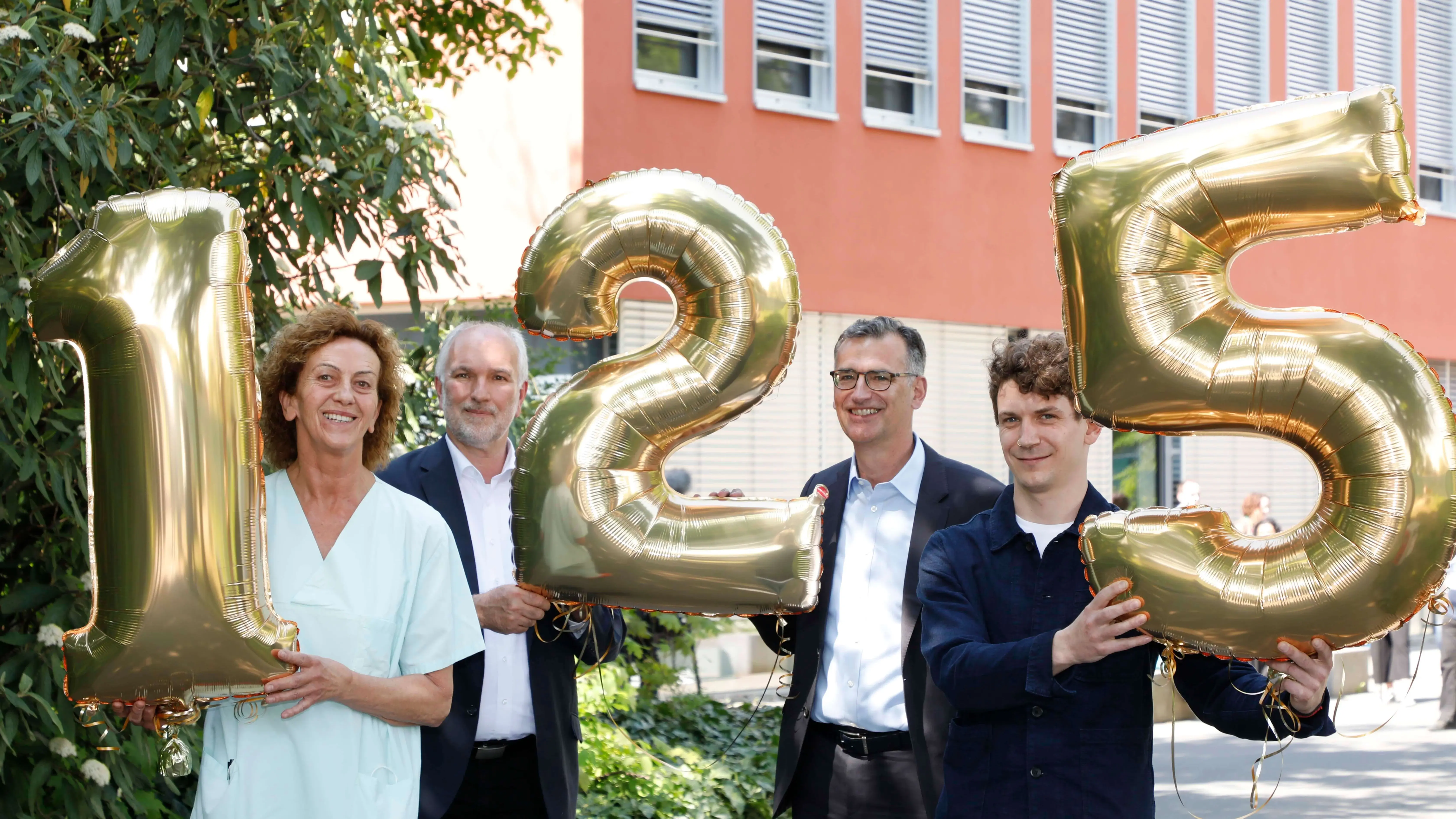 Auf dem Pressefoto sind Prof. Dr. Jockwig, Vorstandsvorsitzender, Peter Schuh, Vorstand Personal und Patientenvertretung, und zwei Mitarbeitende des Klinikums zu sehen. Sie halten goldene Luftballons mit den Zahlen 1,2 und 5 in der Hand. 