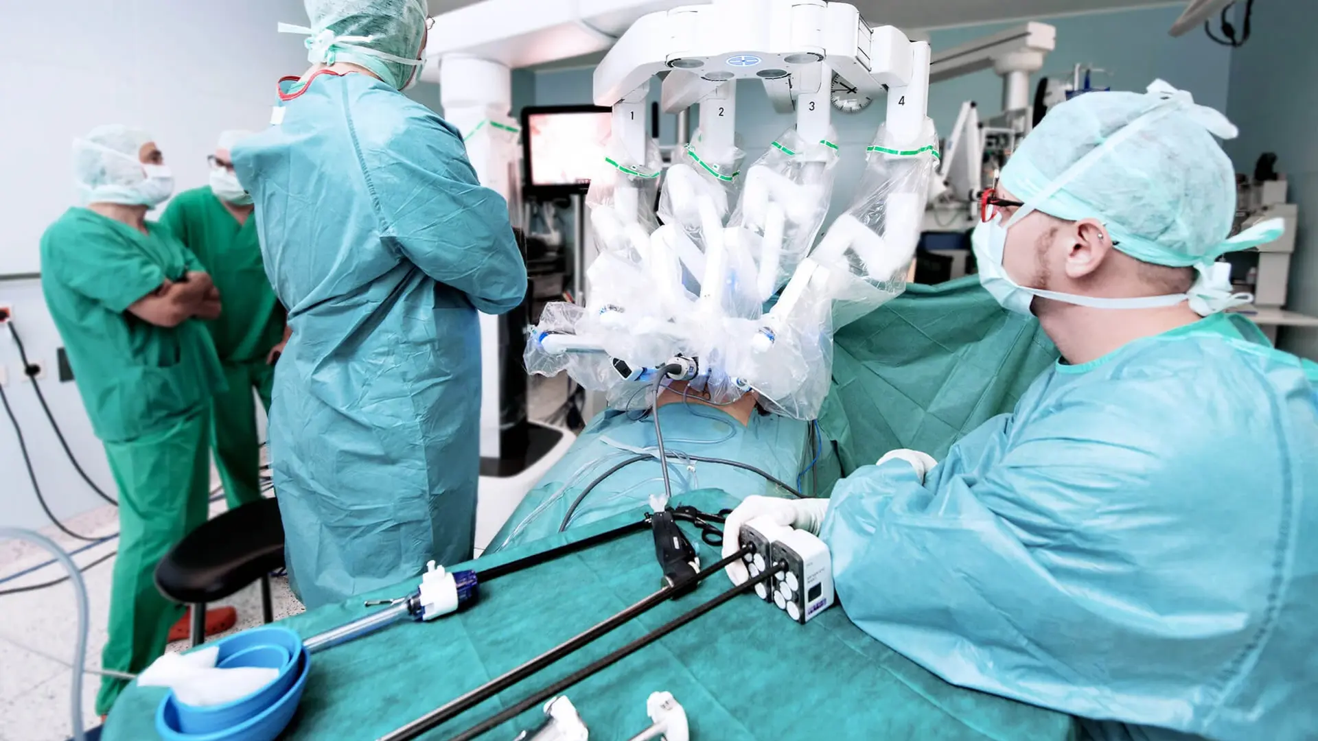 Der Operations-Roboter besteht aus einer Steuerkonsole, an der ein Chirurg sitzt, und einer patientenseitigen Robotikeinheit mit vier Armen und einem Videoturm für die Steuerung der Kamera. 