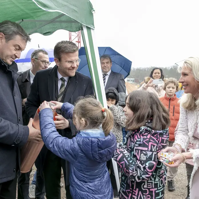 Ministerpräsident Dr. Markus Söder (l.), Oberbürgermeister Marcus König und Schirmherrin Karin Baumüller-Söder geben mit den Kindern ihre Glücksbringer in die Grundsteinrolle.