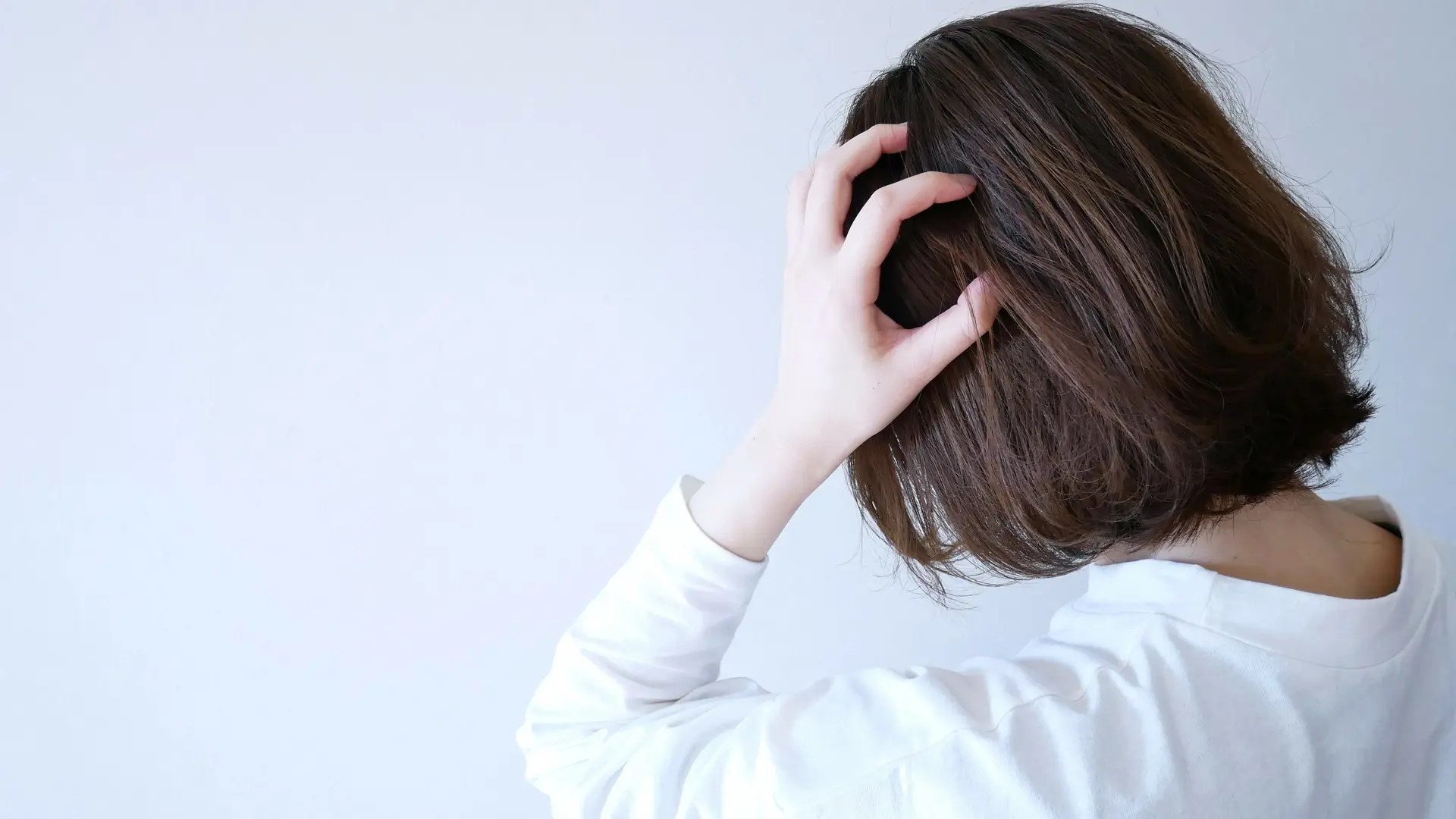 Eine junge Frau greift sich mit der Hand an den Kopf. Ihr Blick ist nicht der Kamera zugewandt.