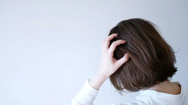 Eine junge Frau greift sich mit der Hand an den Kopf. Ihr Blick ist nicht der Kamera zugewandt.