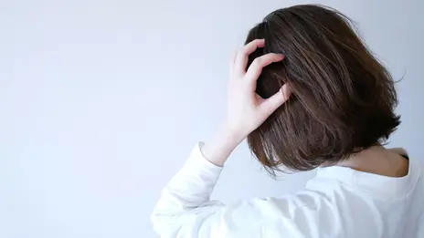 Eine junge Frau greift sich mit der Hand an den Kopf. Ihr Blick ist nicht der Kamera zugewandt.